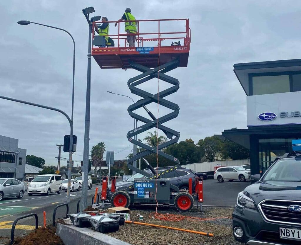 Worker operating a rough terrain scissor lift on a roadside construction site in wet weather conditions in New Zealand